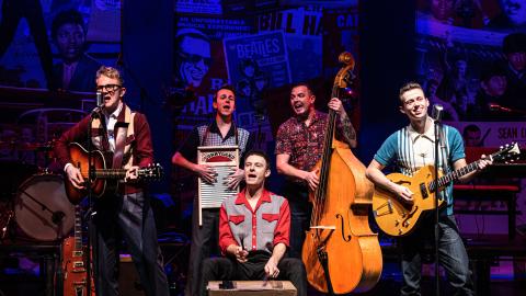 A group musicians on stage singing and playing various instruments.