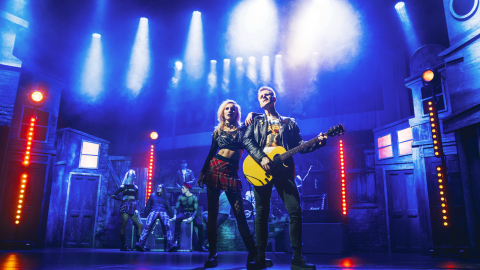 Two musicians in Pretty Vacant stand together in the centre of the stage with blue stage lights shining on them.