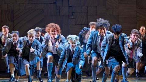 A group of school pupils in uniform on stage against a black background.