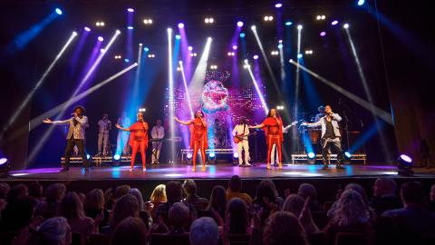 A group of musicians performing on stage, wearing red and white, with bring stage lights shining down on them