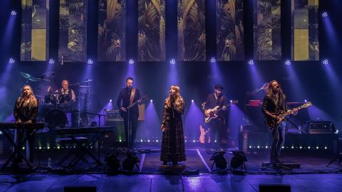 A group of musicians performing on stage as a Fleetwood Mac tribute act with purple stage lights shining down on them.