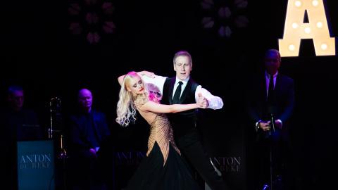 Strictly Come Dancing's Anton Du Beke dances on stage with a woman wearing a black and gold dress.
