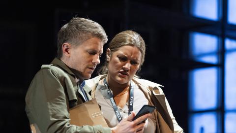 Two actors dressed as casually dressed detectives look at a phone.