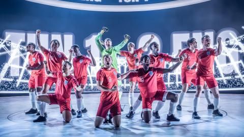 Production image of Dear England with a group of actors dressed a red England football kit.