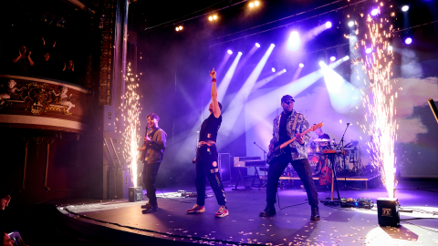 Musicians performing on stage in a Coldplay tribute act, with purple lights behind them and sparks.