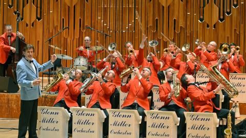 An image of an orchestra playing various instruments while wearing matching orange jackets.