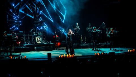 Musicians and singers perform on stage with dramatic dark lighting behind them.