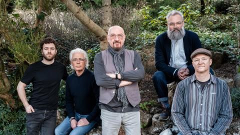 A group of musicians stood outside in a woodland area.