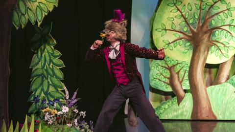 A man in a wolf costume sniffs a yellow flower