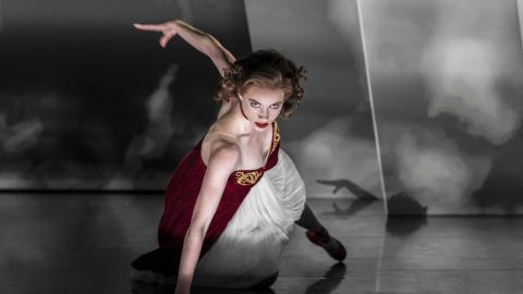 A female dancer with red hair performs in a white dress and red shoes.