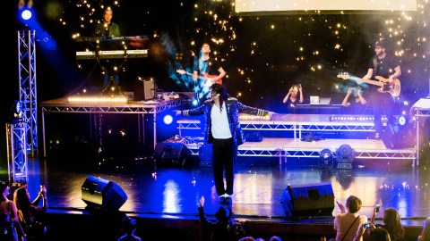 Michael Jackson tribute artist Navi performs on stage with sparks and blue lights behind him.