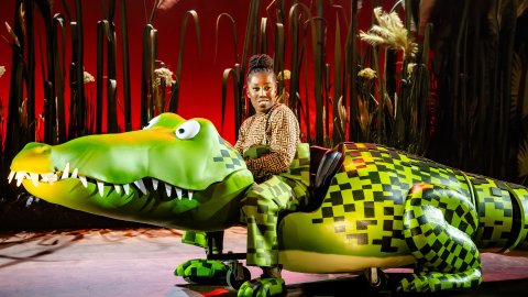 A large puppet of a crocodile with a woman sat in the centre holding the head of the puppet.