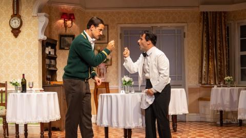 Two men stood in a restaurant setting in a show based on Fawlty Towers.