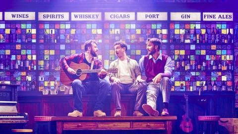 Three men sit on a bar in a pub singing