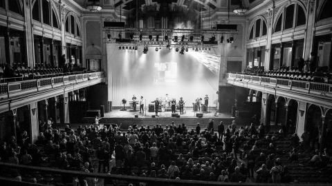 A black and white image of a band performing on stage in front of a crowd.
