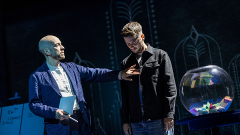 Illusionist Derren Brown stands on stage placing his hand to the chest of a man.