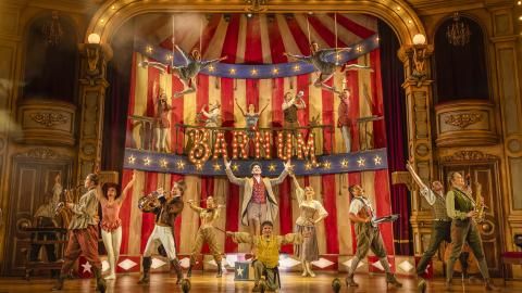 A wide, group shot of the Barnum cast on stage with a large set of a circus tent.