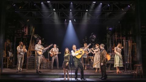 The cast of The Ballad of Johnny and June perform on stage, with a single spotlight shining down on the lead cast in the centre.