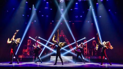 Ballroom dance ensemble performing a choreographed routine on stage under dramatic blue and red lighting.