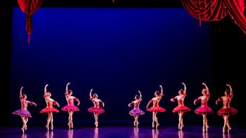 An ensemble of male dancers wearing red outfits on stage against a dark blue background.