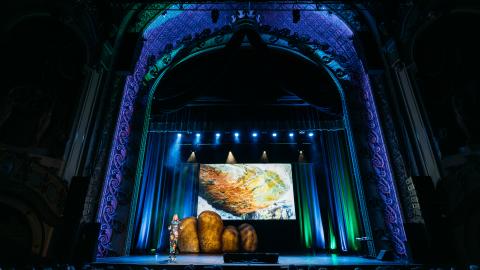 Professor Alice Roberts walks on stage lit with green and blue stage lights.