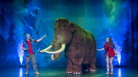 Two actors perform as Rangers on stage in Ice Age Adventure Live, stood between a large puppet of a mammoth.