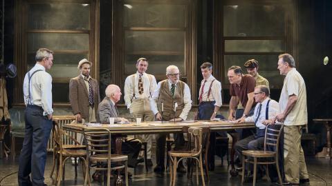 A group of 12 men stood around a long table on the set of Twelve Angry Men.