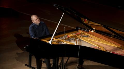 A man in a dark blue shirt plays a grand piano