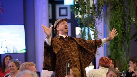A man dressed as Sherlock Holmes talks to dinner guests