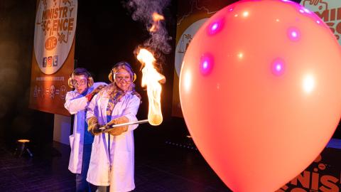 A man and a woman in white lab coats hold fire against a balloon