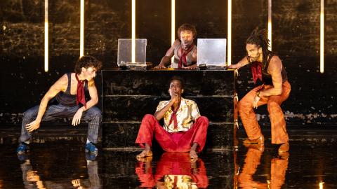 Four men sit on stage during The Brown Suite, wearing 70s inspired outfits.