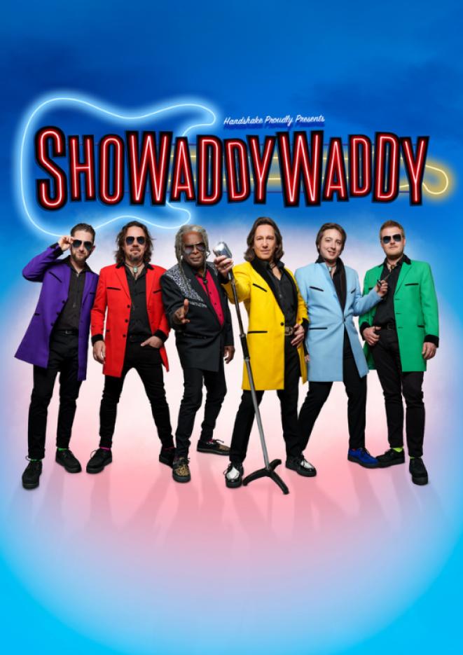 6 members of group showaddywaddy stand against a blue and pink background wearing bright coloured jackets over plain black outfits.