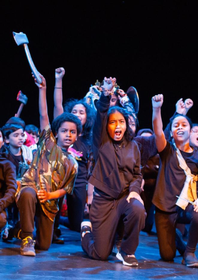 A group of young children on a stage with a black backdrop behind them. 