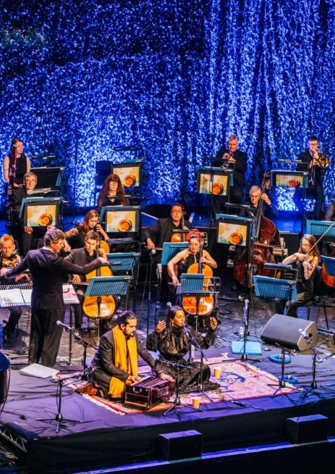 A group of musicians on stage with two singers on the floor of the stage.