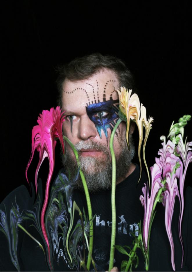 Musician John Grant stands in front of a black background with distorted bright flowers in front of his face.