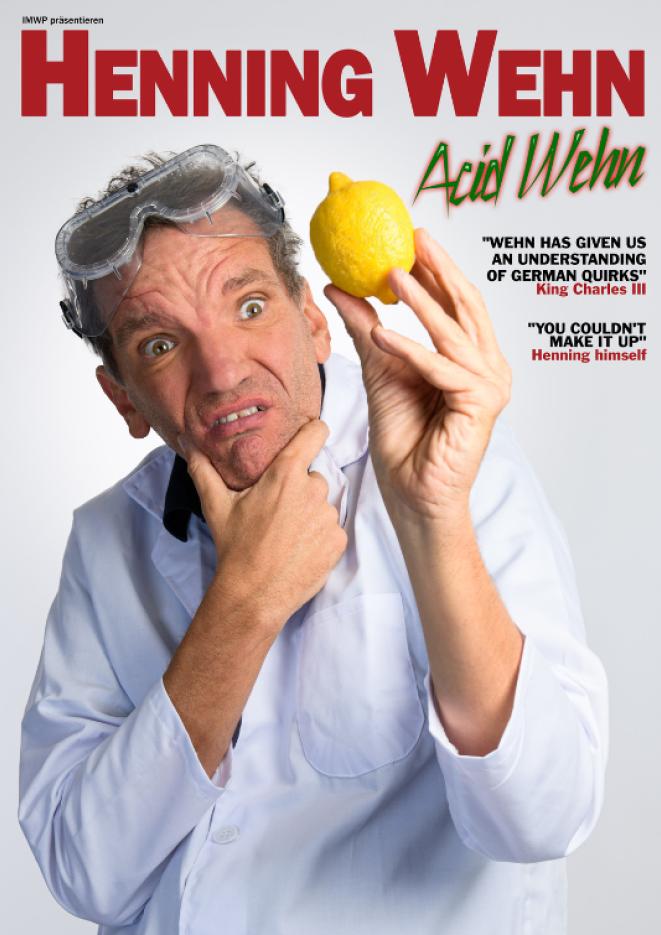 Comedian Henning Wehn stands against a white background wearing a shirt and holding up a lemon.