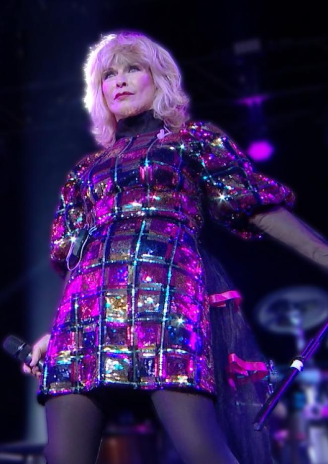 Singer Toyah performs on stage wearing a pink sparkly dress, holding a microphone in her hand.