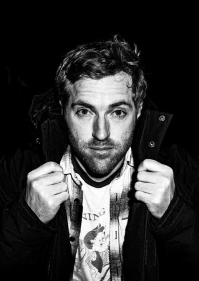 A black and white close up image of comedian Russell Hicks, holding his jacket.