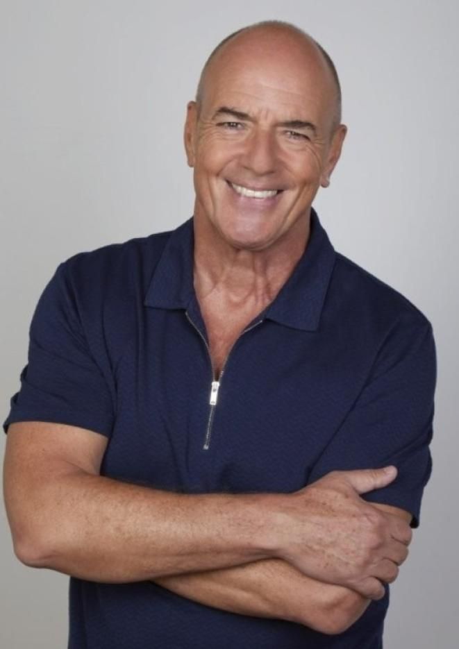 Musician Peter Cox stands against a plain white background with his arms folded.