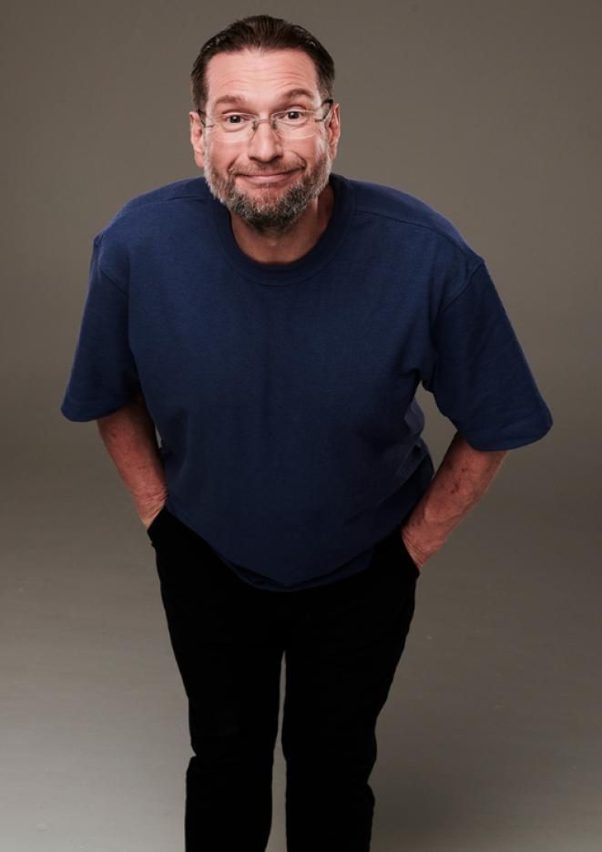 Comedian Gary Delaney stands against a plain, grey background with his hands in his pockets.