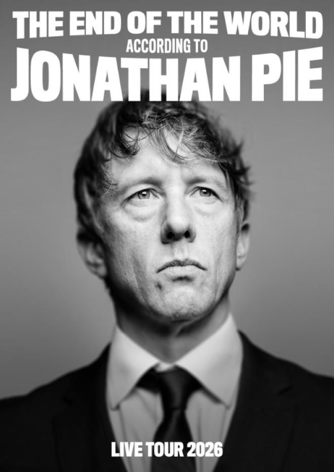 Black and white photograph of Jonathan Pie wearing a suit, staring past the camera