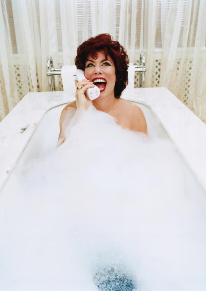 Ruby Wax in a bubble bath laughing into a phone