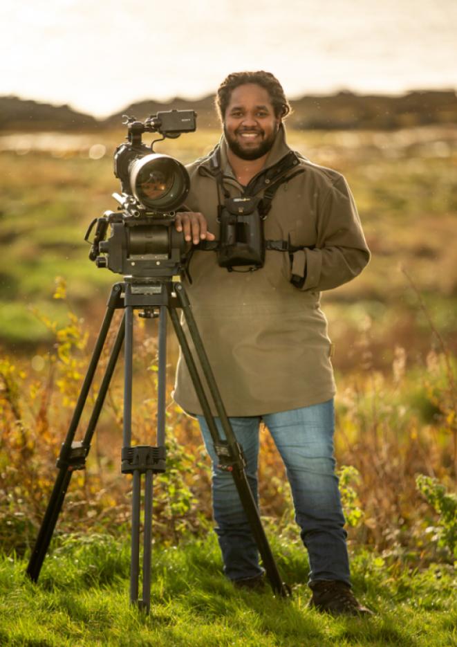 Wildlife photographer Hamza Yassin stands in a meadow standing by his camera on a tripod.