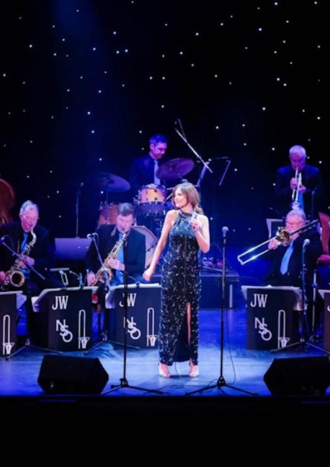A woman in a black evening gown sings in front of a big band