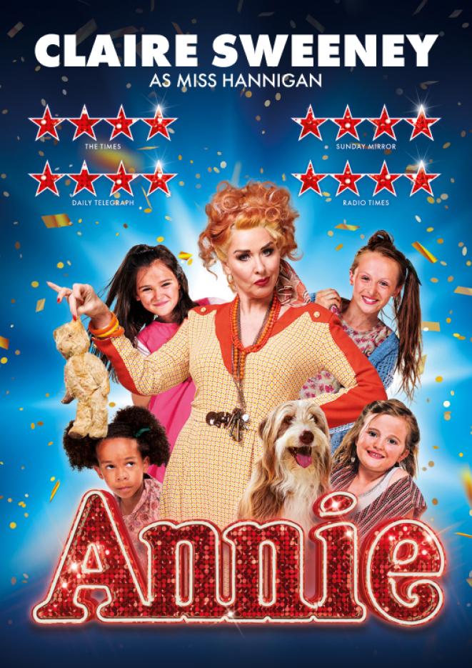 Claire Sweeney looks at the camera in a red and yellow dress holding a toy, with young cast members standing behind her, against a blue background.