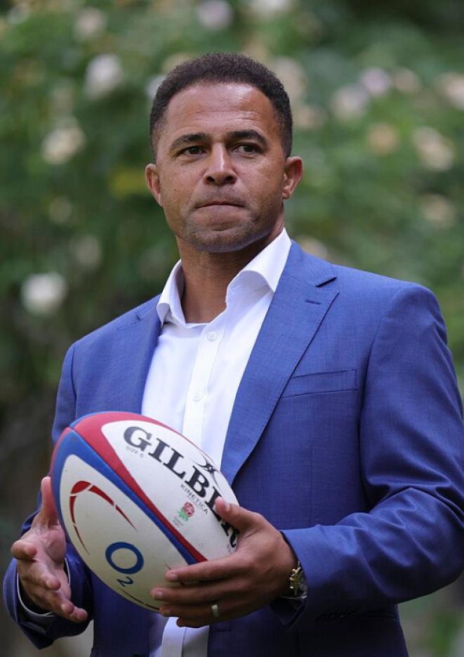 Rugby player Jason Robinson stands wearing a blue suit, holding a rugby ball.