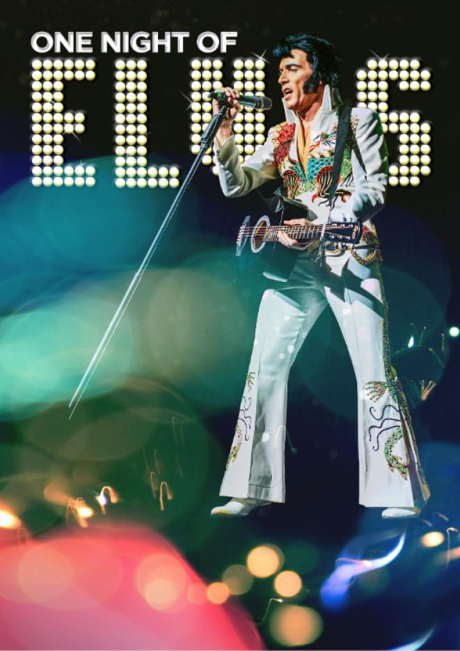 A man dressed as elvis in a white costume sings into a microphone, holding a guitar
