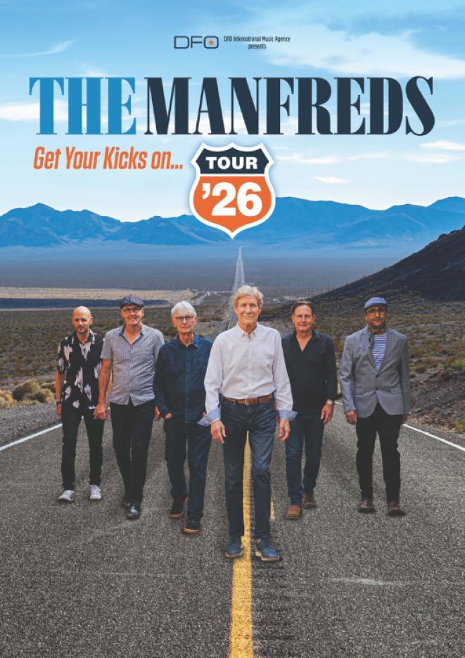 Six members of the band The Manfreds walk along an open road with blue sky and mountains seen in the background.