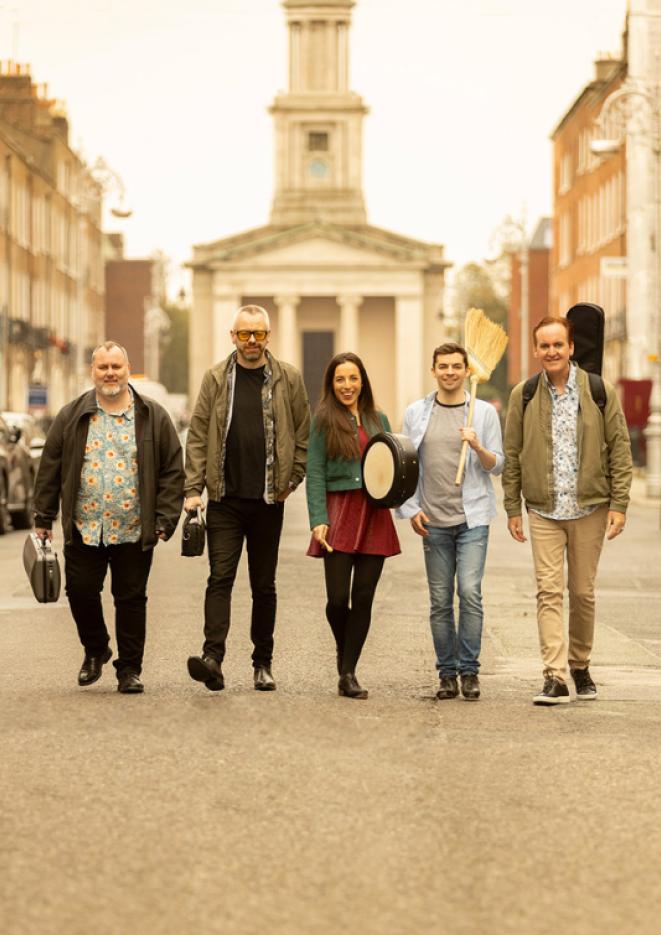 Five musicians stand in the middle of a wide, empty road.