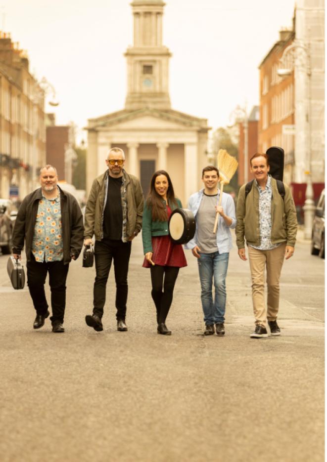 Five musicians stand in the middle of a wide, empty road.